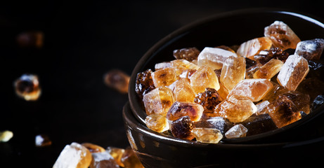 Brown candy cane sugar in clay bowl, black background, selective focus