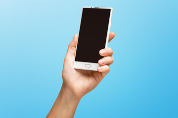 Mockup of female hand holding frameless cell phone with black screen isolated at blue background.