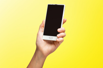 Fototapeta na wymiar Mockup of female hand holding frameless cell phone with black screen isolated at yellow background.