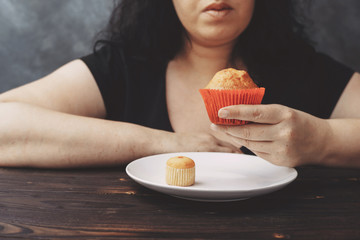 Overweight woman choosing between little and big muffins. Sense of proportion, self control,...