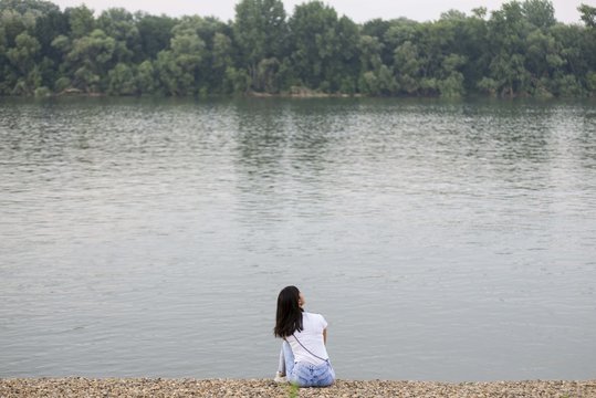 girl from behind sitting on river beach