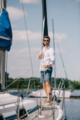full length view of handsome young man in sunglasses standing on yacht