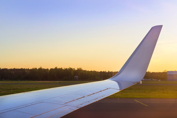 Wing of aircraft over the runway at sunset. Passenger airplane on airport runway, Marupe, Riga, Latvia. Road transport infrastructure of international airport