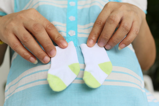 Pregnant mothers holding a small pair of socks on stomach.