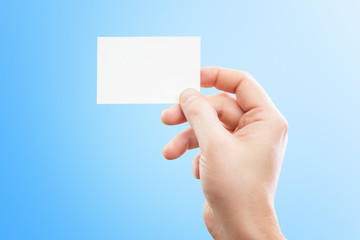 Obraz premium Male hand holding white business card at isolated blue background mockup.