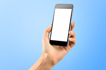 Female hand holding black cellphone with white screen at isolated blue background.