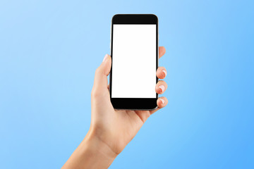 Female hand holding black cellphone with white screen at isolated blue background.