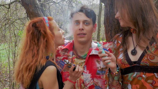 Hippie girls and boy has a fun with e-cigarette smoke in the picnic at spring park 