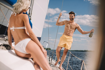 handsome shirtless man with bottle of champagne and his girlfriend on yacht