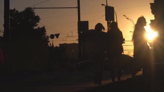silhouettes of people,  and cars on the urban street  at sunset