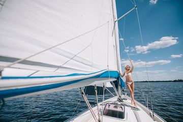 Fototapeta na wymiar distant view of attractive young woman in swimwear standing on yacht