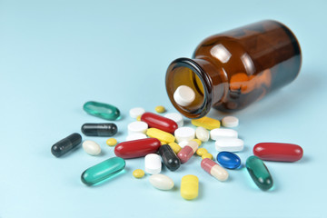 Assorted medicine pills pouring out of the brown bottle on blue background.