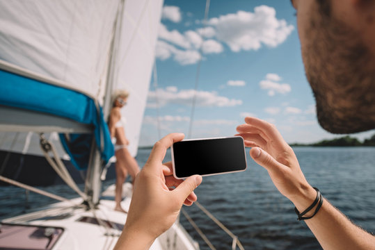 cropped image of man taking picture of girlfriend on smartphone on yacht