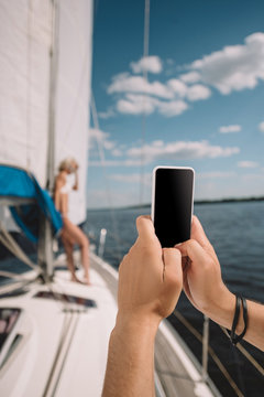 cropped image of man taking picture of girlfriend on smartphone on yacht