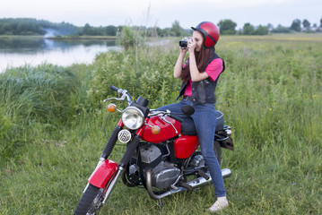 Fototapeta na wymiar Girl in a retro helmet sitting on a vintage motorcycle with a camera