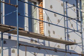 The process of building wall insulation using polystyrene in the open air. Scaffold on house, renovation. House for renovation with the scaffolding for workers on building