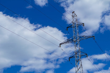 Electric high voltage tower with electric line against clouds blue sky