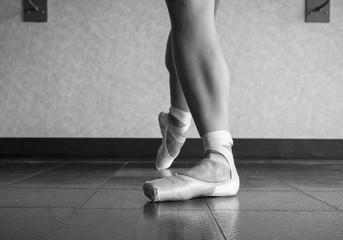 Black and white version of Ballet dancer showing off her pointe shoes standing in classical position
