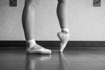 Black and white version of Ballerina warming up her feet in her pointe ballet shoes before class