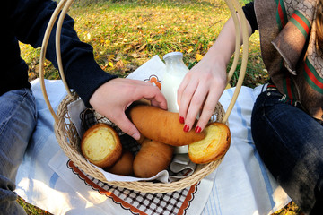 wicker basket for a picnic with pies, cheesecakes, a beautiful ceramic mug and a bottle of milk. Male anf female hand takes the same pie. Moscow region, Russia.