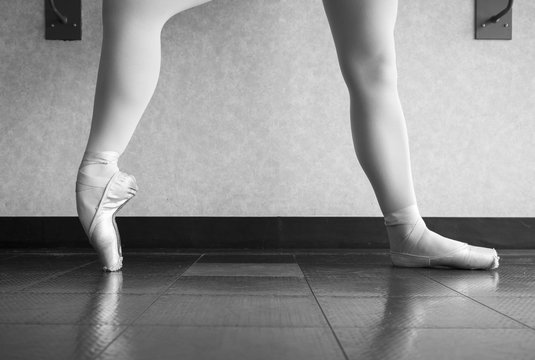 Black and white version of Ballerina in ballet class warming up he pointe shoes, ballet slippers at the barre
