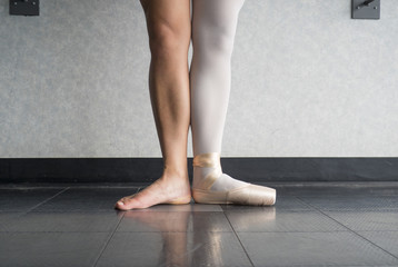 Ballet dancer in first position with one foot in a pointe shoe, and one bare leg © Katherine BYC