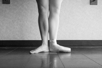 Black and white version of a ballet dancer in first position with one foot in a pointe shoe, and one bare leg