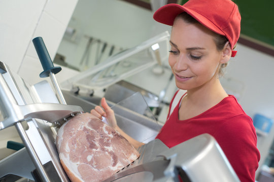 woman pork butcher cutting cooked ham with machine