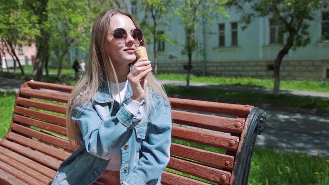 Young girl sitting on a bench with ice cream on her hands, wearing a white t-shirt, denim, jeans and sunglasses