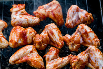 Spicy marinated chicken wings grilling on a summer barbecue with hot flames in a close up view