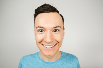 Close up portrait of young smiling man dressed in a blue t-shirt on a light background.