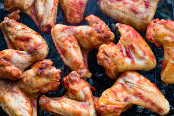 Spicy marinated chicken wings grilling on a summer barbecue with hot flames in a close up view