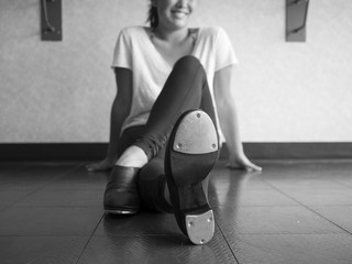 Black and white version of Smiling teenage tap dancer sitting cross legged in dance class relaxing 