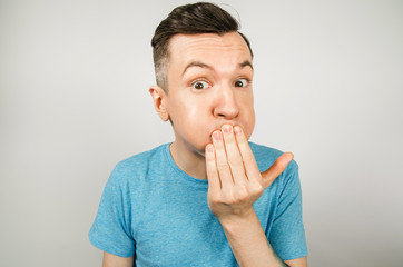 Young guy dressed in a blue t-shirt closing mouth from vomiting on a light background.