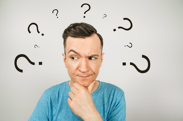 Young thinking man dressed in a blue t-shirt on a light background.