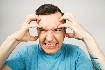Young guy with headache dressed in a blue t-shirt on a light background.
