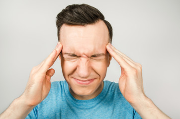 Young guy with headache dressed in a blue t-shirt on a light background.