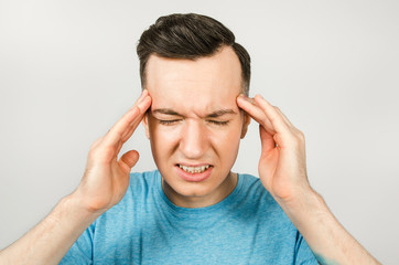 Young guy with headache dressed in a blue t-shirt on a light background.