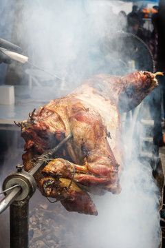 Cook's hand with a knife checks the readiness of the lamb on a spit in the smoke over hot coals. Outdoor grill