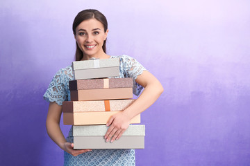 Beautiful young woman with many gift boxes on color background