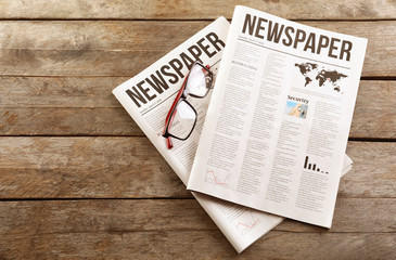Naklejka premium Newspapers with glasses on wooden background