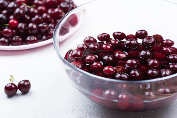 Summer concept. The process of washing a ripe red cherry. Cherry in a bowl of water on a white concrete background. Design Copy Space Close-up..
