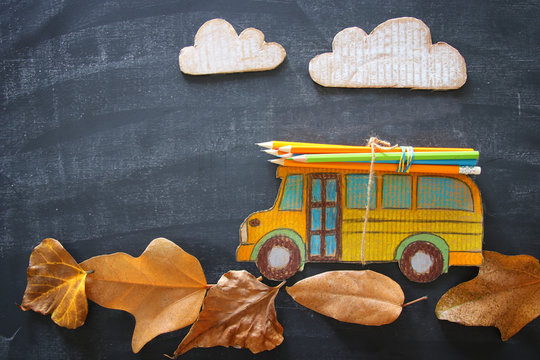 Back to school concept. Top view image school bus and pencils over autumn dry leaves classroom blackboard background.