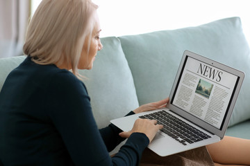 Mature woman reading news on laptop screen at home