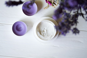 Lavender flowers, candles and cream on a white wooden background. Beauty care.