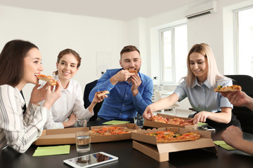 Young people eating pizza at table in office