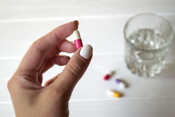 A capsule in female hand and glass of water on a white table.