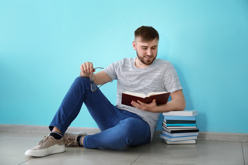 Young man reading book while sitting near color wall