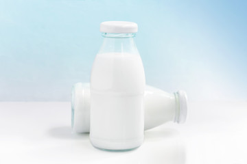 Two glass bottle of milk on the white table on a blue background. with copy space for text.