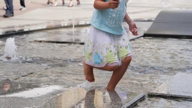 Barefoot child girl legs walk the city street fountain shallow water in hot day